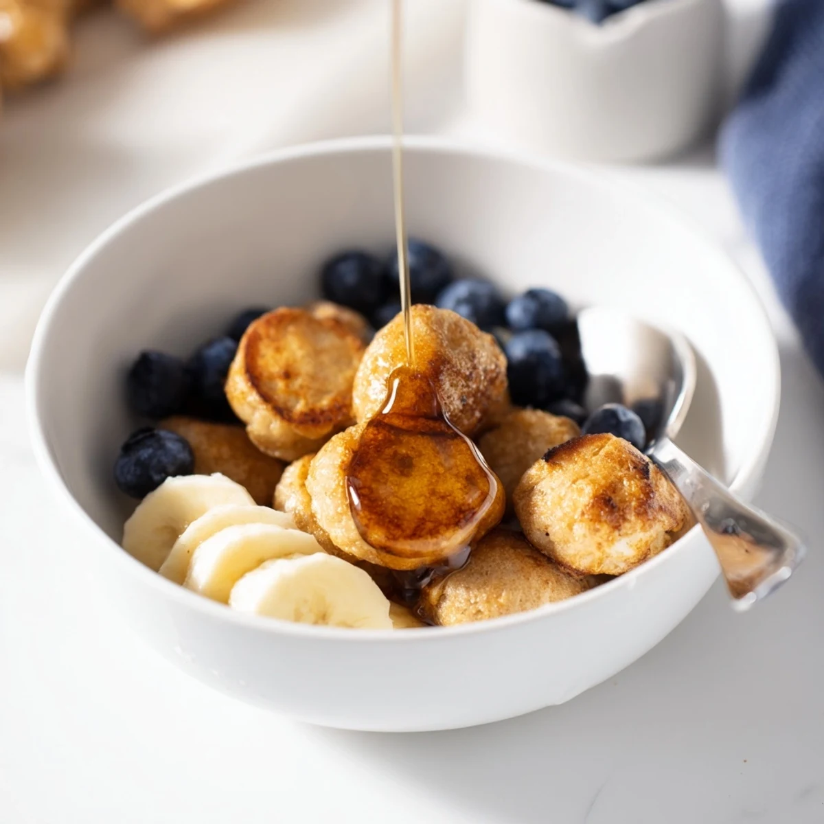 Delicious mini pancake cereal served with syrup and fresh berries in a bowl.  