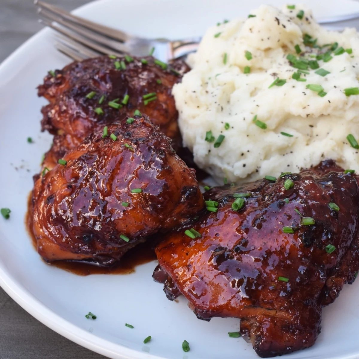 Succulent honey BBQ chicken thighs drizzled with sauce, served alongside fluffy garlic mashed potatoes.  