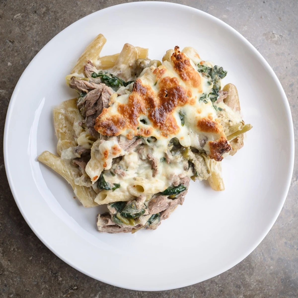 Steak & Spinach Artichoke Pasta Bake bubbling with golden mozzarella, inviting you to enjoy this comforting, hearty dish.