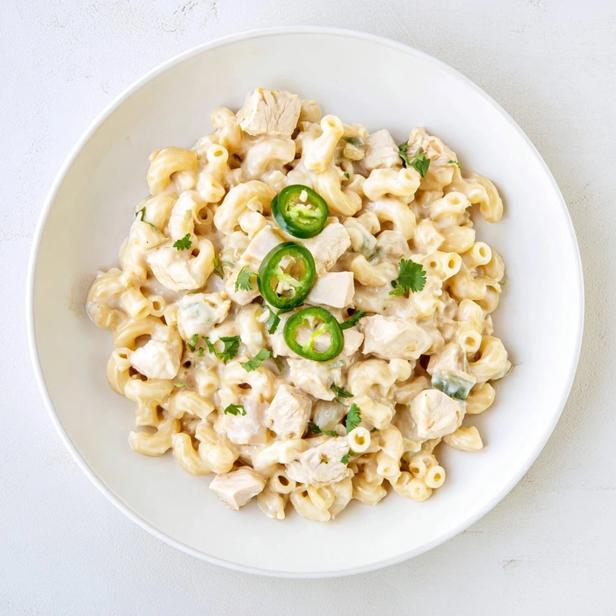 A spoon lifts a cheesy serving of Green Chili Chicken Mac, showcasing tender chicken pieces and mild diced green chiles throughout.