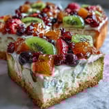 Festive dessert pizza with sugar cookie crust, smooth cream cheese frosting, and a rainbow of fresh seasonal fruits arranged in a cheerful pattern.  