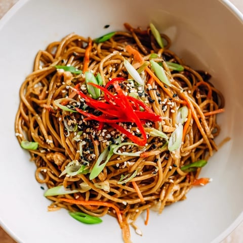 Steaming Asian Garlic Noodle Bowl topped with sesame seeds and fresh green onions, ready to eat.