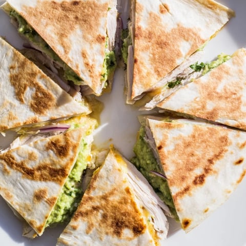 Golden-brown Chicken Avocado Quesadilla wedges reveal layers of grilled chicken and creamy avocado mash.