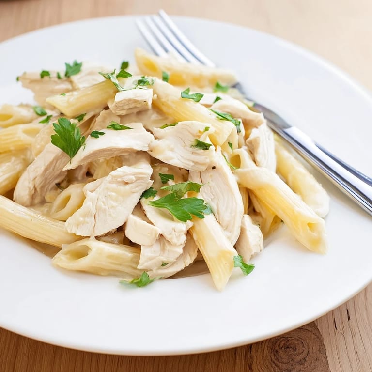 Steam rises from a serving of Roasted Garlic Chicken Penne, garnished with fresh parsley and a generous sprinkle of Parmesan cheese.