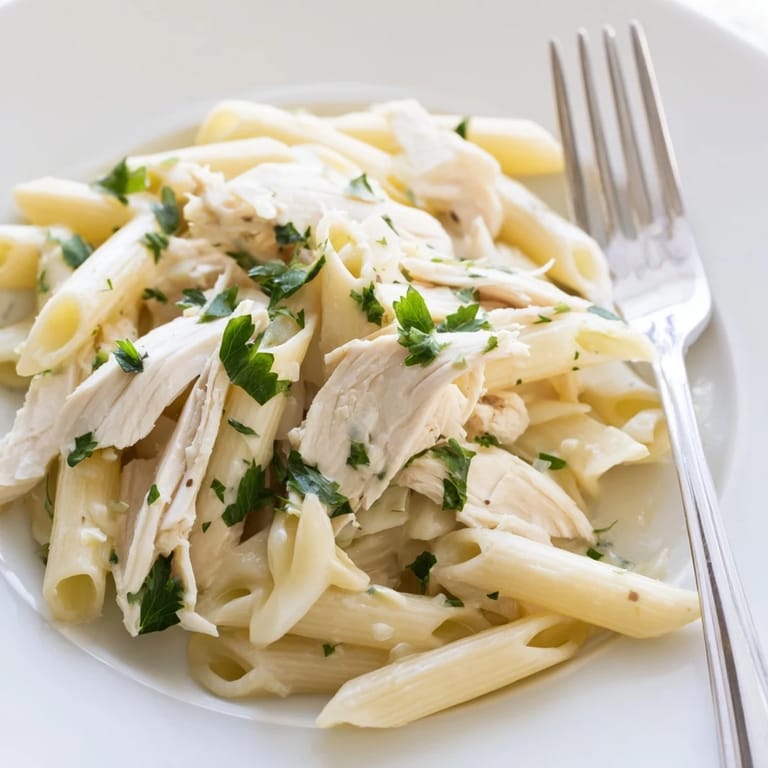 A rustic wooden bowl holds Roasted Garlic Chicken Penne, highlighting the juicy chicken and rich, oven-roasted garlic cream sauce.