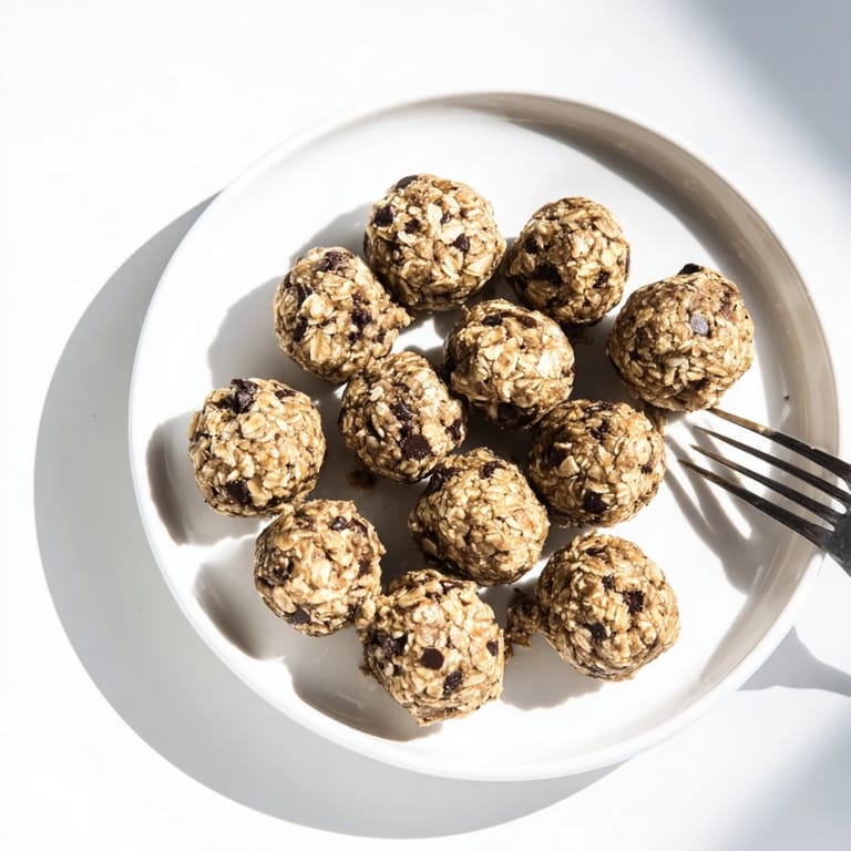 Freshly rolled Banana Chocolate Chip Energy Balls sit on a white plate, with mashed banana and oat ingredients nearby for context.