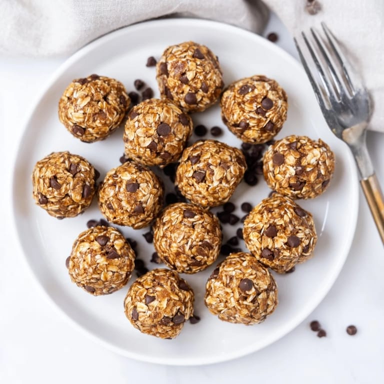 A hand holding a bite-sized Banana Chocolate Chip Energy ball reveals its soft, crumbly interior studded with chocolate chips.