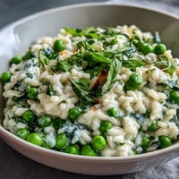 A creamy spring pea and mint risotto topped with Parmesan cheese, served in a white bowl with fresh mint garnish.
